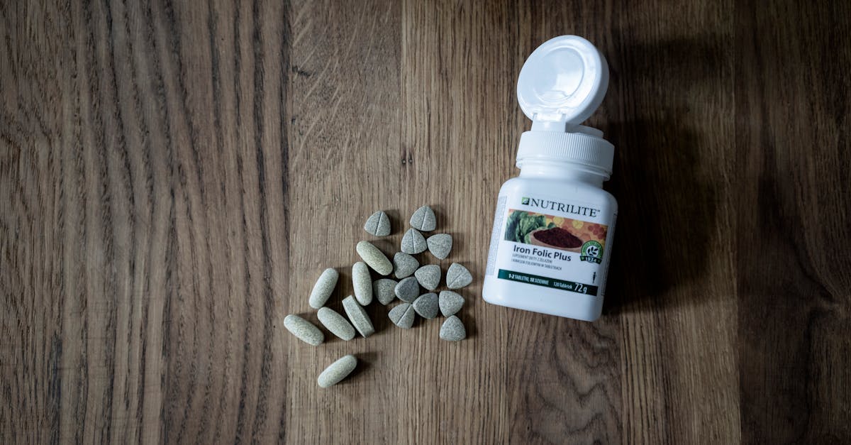Open bottle of Iron Folic Plus tablets with scattered pills on a wooden surface.